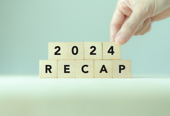2024 Recap economy, business, financial concept. Business planning in 2025. RECAP text on wooden blocks and hand  placing of 2024  on wooden blocks on minimal grey background and copy space.