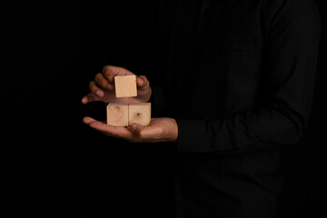 Businessman holding wooden block on black background. Risk management concept, Hand holding wooden...