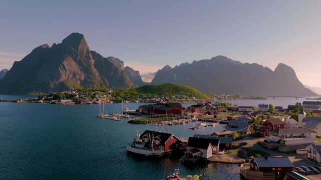 A picturesque coastal village in Norway unfolds, showcasing vibrant red cabins, boats bobbing gently in the water, and majestic mountains illuminated by the warm glow of sunset. Reine village Lofoten