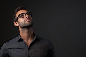 Obraz premium Confident Young Man in Glasses Looking Up Against a Dark Background