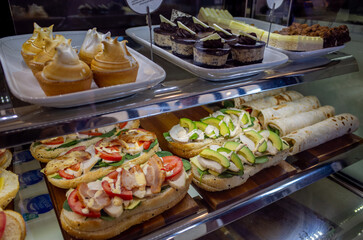 A bakery or café counter with a tempting display of fresh pastries, sweet cakes, sandwiches, and wraps. A typical breakfast and dessert selection in Australia.