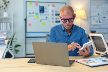 Senior manager sitting at desk in office, using calculator and laptop to analyze financial data, demonstrating concentration and expertise in business management