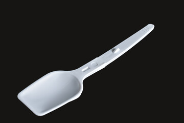 A white disposable plastic spoon lies on a black background.