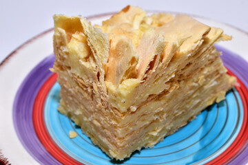 A large piece of layered cake called Napoleon with cream lies on a plate.