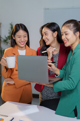 Three young businesswomen smiling and collaborating on a laptop in a modern office, engaging in productive discussions and strategizing effectively for their project