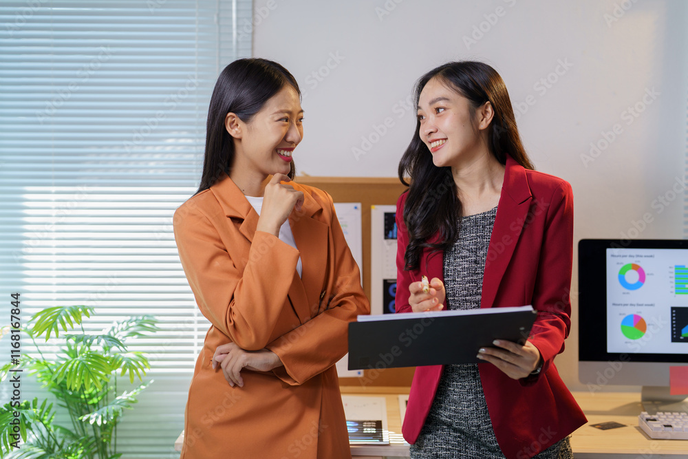 Poster two young businesswomen are discussing work in a modern office, smiling and holding a folder while r