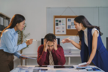 Two furious female coworkers are aggressively criticizing a male colleague, causing him great...