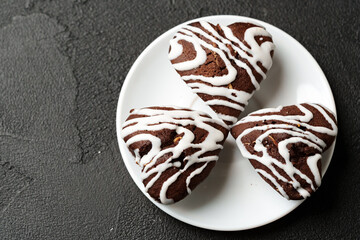 Delicious heart-shaped chocolate cookies with white icing on a plate