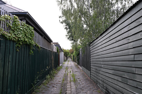 Narrow cobbled bluestone laneway in suburban Melbourne, with green wooden fences on either side of the lane, during an overcast day