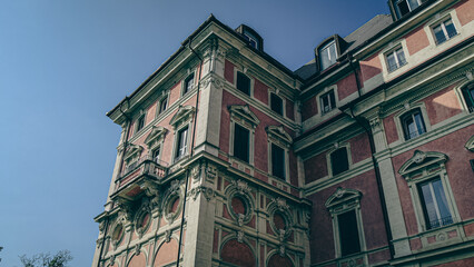 A historic red brick estate with stone window accents and an ornate central entrance. Surrounded by bare autumn trees and classic street lamps, the building’s grandeur contrasts with quiet courtyard E