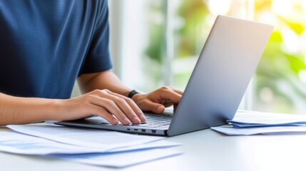 A person working on a laptop with papers on a desk.
