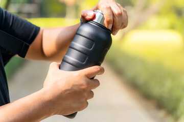 Naklejka premium A person wearing a black shirt opening a black water vacuum flask in a park setting