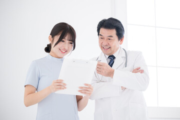 カルテを見て医師と話す笑顔の看護師　申し送りや治療計画のイメージ