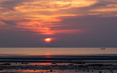 A vivid red sunset casts its glow over a sandy beach with scattered rocks.