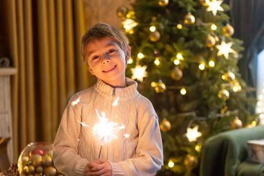 School child, boy, standing at home on christmas, holding sparkler in front of the Christmas tree