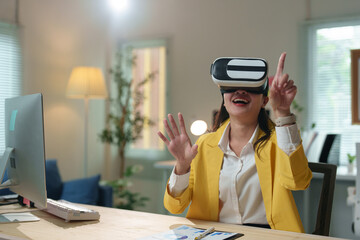 Young businesswoman wearing vr headset is sitting at desk in modern office, interacting with virtual reality and gesturing with hands, enjoying innovative technology