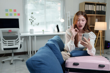 Young asian woman is sitting on a sofa in her home office, making an ok gesture while looking at...