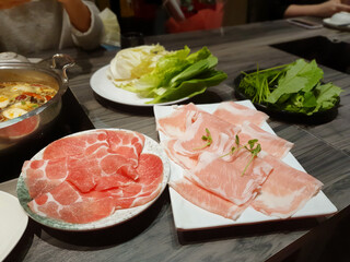 Delicious hot pot eating at a restaurant, Chinese and Japanese hot soup beef meat and pork sliced in plate, cabbage vegetable in white bowl, traditional food stock photo