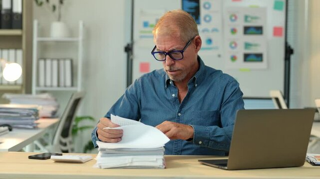 Office worker carefully examines a stack of papers, meticulously sorting and reviewing each document with focused attention, demonstrating professionalism and diligence in his administrative tasks