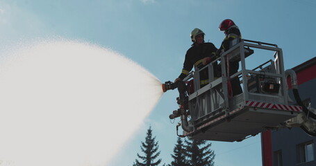 Firefighters stand in a special lifting cradle and put out a fire with a fire hose. The footage shows hard work in extreme conditions. Ideal for themes about rescue operations.