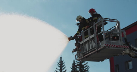 Firefighters stand in a special lifting cradle and put out a fire with a fire hose. The footage shows hard work in extreme conditions. Ideal for themes about rescue operations.