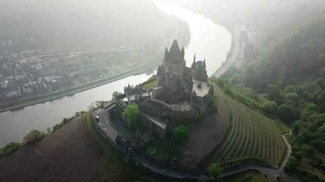 Reichsburg, a medieval castle overlooking the Moselle river and Cochem, rises majestically from a hilltop, shrouded in morning mist for a picturesque scene, establishing shot