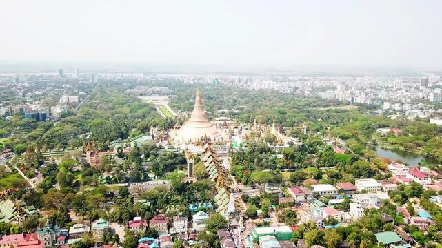 Aerial view captures the sprawling landscape of Rangun, Myanmar, showcasing the numerous buddhist temples and pagodas interspersed with lush greenery and the cityscape in the background