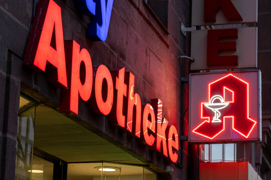 Das Bild zeigt ein beleuchtetes Apotheken-Schild in einer deutschen Stadt.