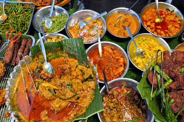 Close-up of a variety of Nasi Lemak dishes with traditional side dishes, curries, and fried accompaniments displayed at a local food stall.