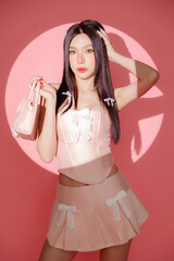 Trendy Beautiful confident Asian woman in pink sexy dress with perfect slim body clean fresh skin holding handbag in lighting studio. Fashionable female model.