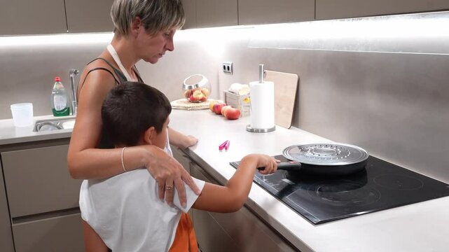 Caring mother guiding son while preparing popcorn together, demonstrating patient teaching and family bonding on modern induction stove in bright kitchen