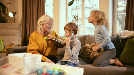 Boy uses stethoscope on grandmother while girl observes, fostering understanding of listening to...