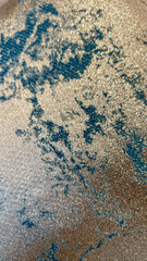 Close-up of a luxurious textured fabric with shimmering gold and teal patterns, showcasing intricate details and a refined aesthetic. Perfect for highlighting elegance and premium textile design.