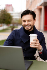 Smiling young businessman holding coffee while working with laptop outdoors