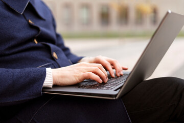 Close up of businessman hands typing on laptop sitting in the city