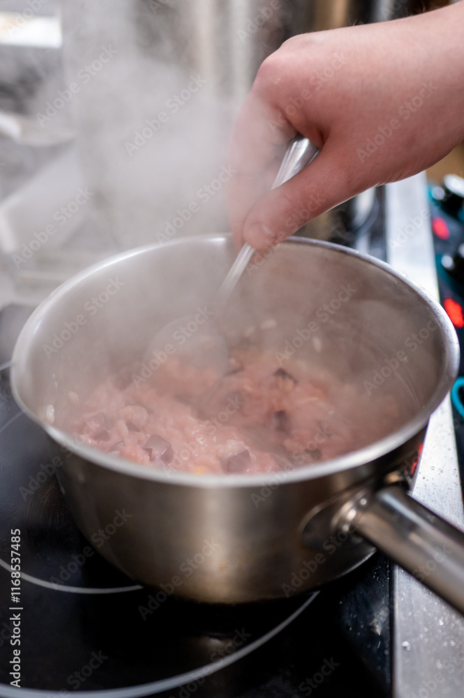 Wall mural A hand stirs a pot of steaming risotto on a stovetop. The creamy rice dish has hints of pink and is surrounded by rising steam, indicating a warm, inviting cooking scene.