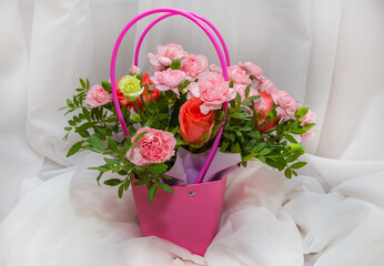 Pink basket with a bouquet of flowers from roses and carnations on a white background made of fabric.