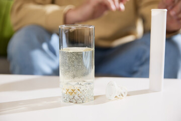 Close up of glass with dissolving vitamin tablet that makes bubbles water and plastic tube of medicines nearby. Concept of illness, health insurance, pharmaceutical, medicine. Ad.