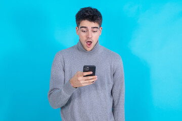 surprised young man with mobile phone or smartphone isolated on blue background