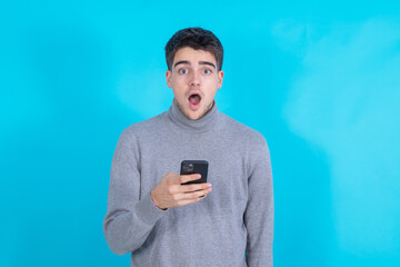 surprised young man with mobile phone or smartphone isolated on blue background
