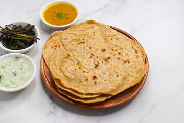 Roti and Sabzi. Indian vegetarian Thali includes bhindi fry, yellow daal tadka, cucumber raita, and chapati or tel paratha. Indian food is served in a plate or thali. Copy Space. healthy Veg Thali. 