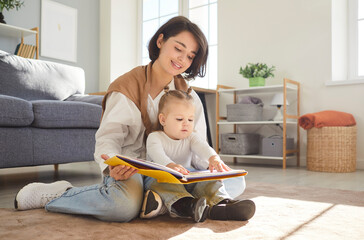 Loving happy young mother, babysitter and little child reading book, funny story playing together...