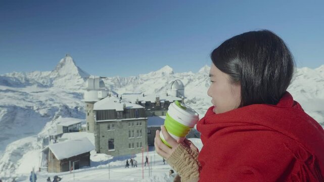 A serene winter scene featuring a woman enjoying a warm drink amid snow-covered mountains. The picturesque backdrop enhances the cozy atmosphere, perfect for a moment of relaxation during a snowy geta