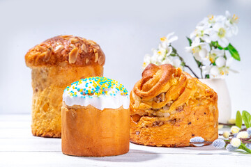Easter baking background with traditional holiday cakes - kraffin, panettone, paska kulich, with Easter eggs, spring flowers on white wooden table, spring holiday Easter greeting card background