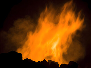 Intense orange flames and smoke rise against a dark background, depicting the burning of fossil fuels like coal or oil. Close-up detail highlights the heat, energy, and pollution 