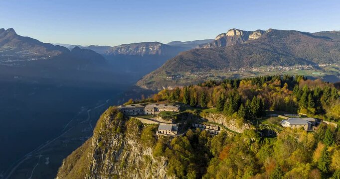 Aerial scene showcasing the historical fortress of Punta Corbin, located in Vicenza, Italy, amidst breathtaking mountainous terrain and lush greenery.