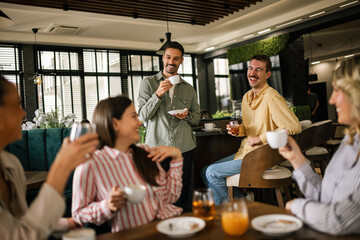 Group of female friends drinking coffee at the restaurant while the guys in the back try to flirt and send them drinks.