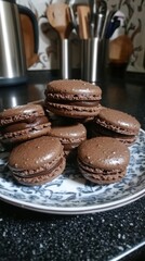 Chocolate macarons on a plate on a kitchen counter.