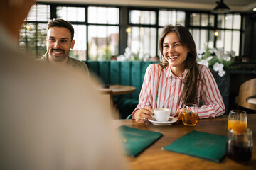 Fototapeta premium Group of young people sitting at a table in a modern café, enjoying their time together with cups of coffee and glasses of freshly squeezed juice.
