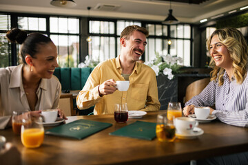 Group of young people sitting at a table in a modern café, enjoying their time together with cups of coffee and glasses of freshly squeezed juice.